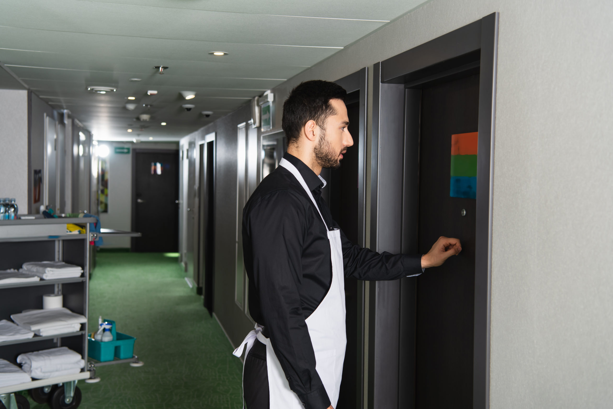 side view of bearded housekeeper knocking door in hotel room