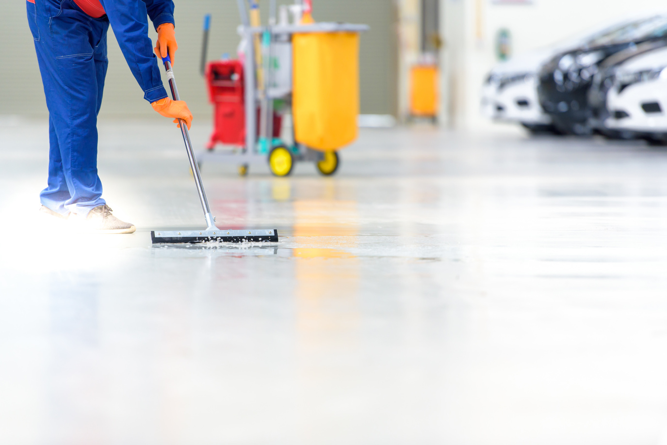 The car mechanic is cleaning, using a mop, rolling water from the epoxy floor. In the car service repair center